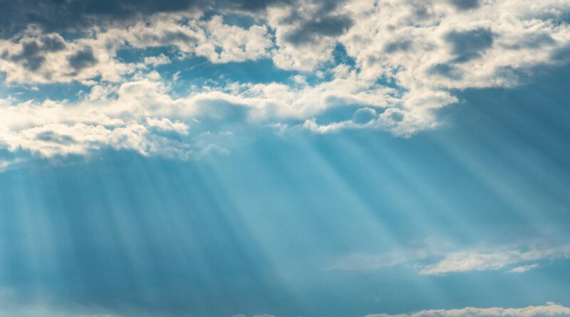 Vibrant sunrays pierce through a cloudy sky, creating a dramatic and dreamy cloudscape.
